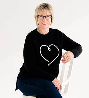 Deb Crowe in a black sweater sitting on a chair.